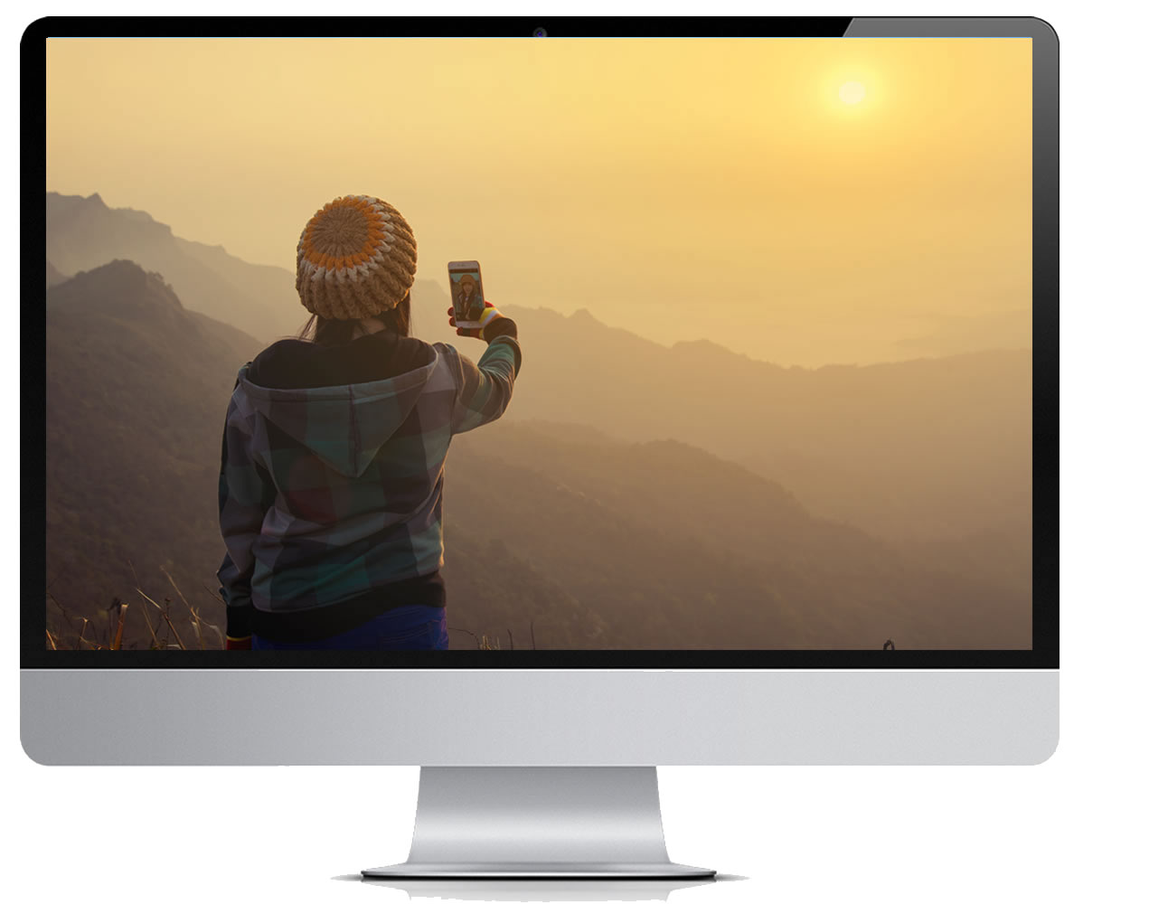 Computer Monitor with a person taking a picture of a sunset over a maountainscape