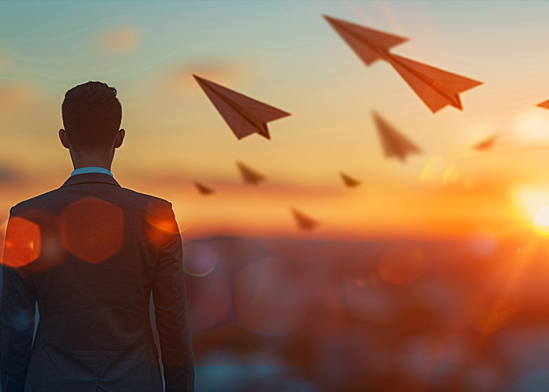 Business Man Looking into the sunset with paper airplanes flying around him